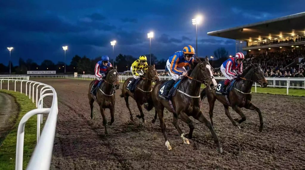 Horses racing on a Polytrack all-weather surface under floodlights at a UK racecourse